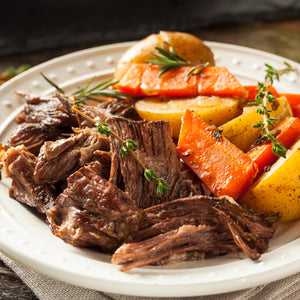 Plated dish of braised meat served with carrots and potatoes on a wooden table.