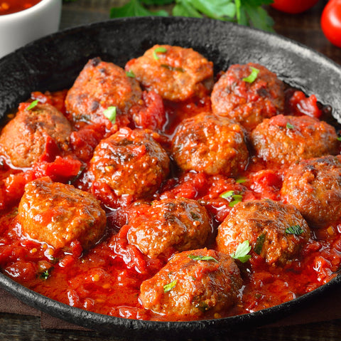 Black skillet with meatballs in a red sauce on a wooden surface