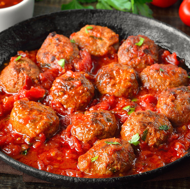 Black skillet with meatballs in a red sauce on a wooden surface