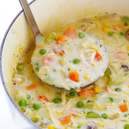 A spoon ladling out chicken pot pie soup filled with vegetables, from a pot.