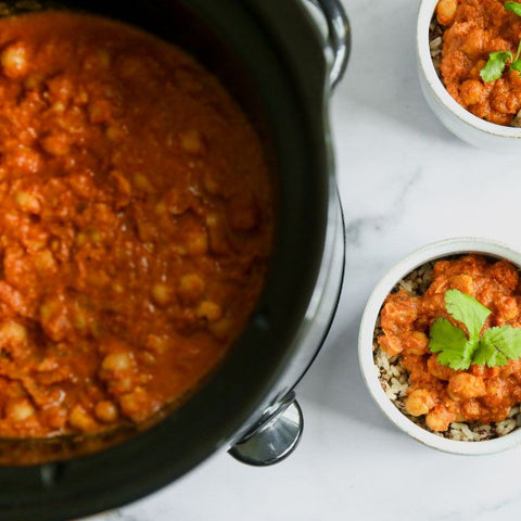A bowl of Indian Butter ChickPeas served over rice with a garnish of cilantro, alongside a crockpot.