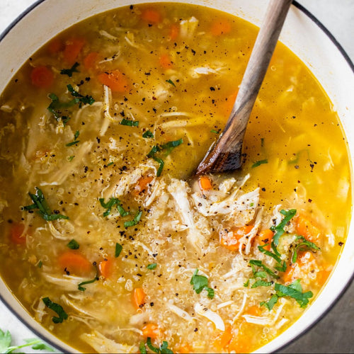 A bowl of Lemon Quinoa Chicken Soup with a spoon, containing chicken, carrots, celery, quinoa, and kale, garnished with parsley.