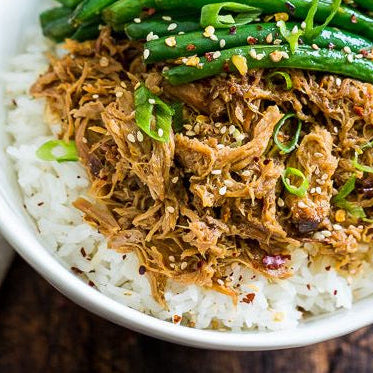 A bowl of pulled chicken over white rice, garnished with green onions and sesame seeds, with steamed green beans on the side.