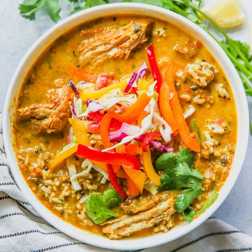 A bowl of Caribbean Pork Curry topped with sliced peppers and cilantro, served over rice.