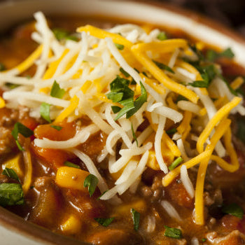 A bowl of Chicken & Chorizo Chili topped with shredded cheese and chopped herbs.