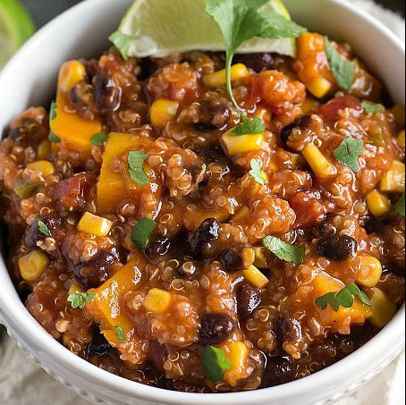 A bowl of quinoa enchilada mixture topped with chopped cilantro and a slice of lime.