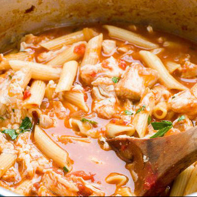 A bowl of Fire Roasted Tomato, Penne & Chicken Soup with a wooden spoon.