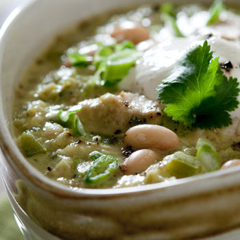 A bowl of Roasted Green Chili, Zucchini & Bean Stew garnished with cilantro and a dollop of sour cream.