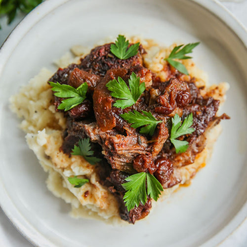 A plate of pomegranate pot roast served over mashed potatoes, garnished with parsley.