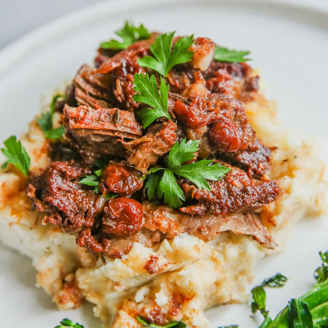 A plate of Moroccan pot roast served over mashed potatoes, garnished with parsley.