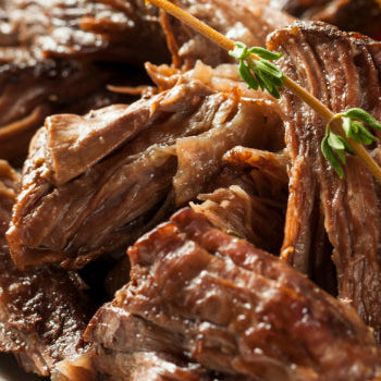 A close-up image of a pot roast dish, showcasing the meat with pieces of mushrooms and herbs, garnished with thyme.