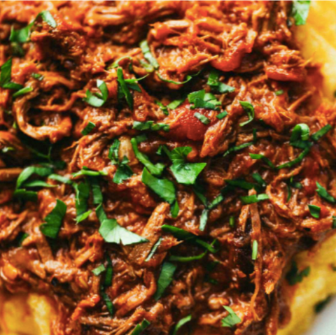 A close-up image of a rustic beef ragù with San Marzano tomatoes served over pasta, garnished with chopped parsley.