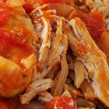 Close-up of a plate containing Moroccan chicken stew with tomatoes and spices, served over rice.