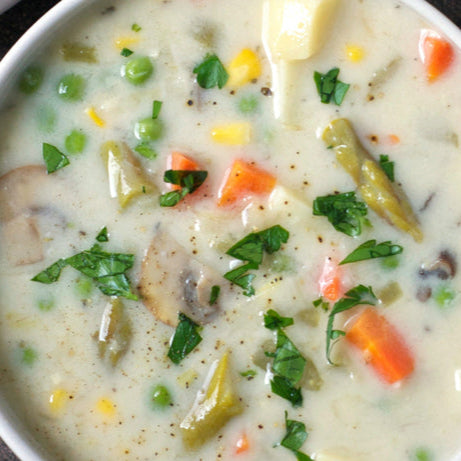 A bowl of vegetable pot pie soup, topped with chopped parsley.