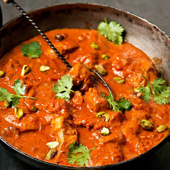 A pan of Tikka Masala with chicken, tomatoes, and spices, garnished with cilantro leaves.