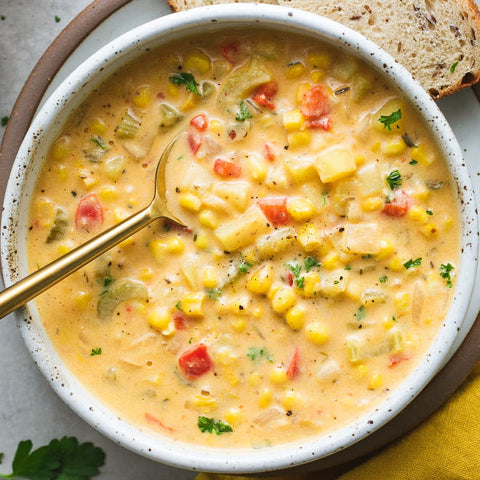 A bowl of Vegetable Corn Chowder with a spoon resting in the bowl, and a piece of bread in the background.